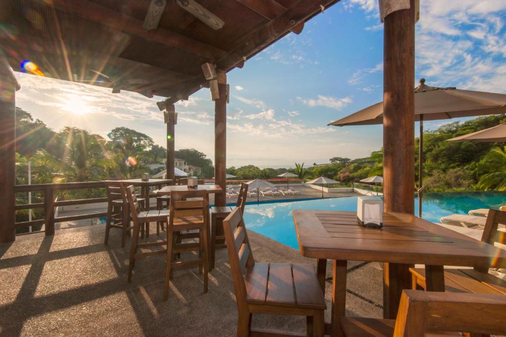 Covered bar area with wooden furniture overlooking pool and landscape at sunset.