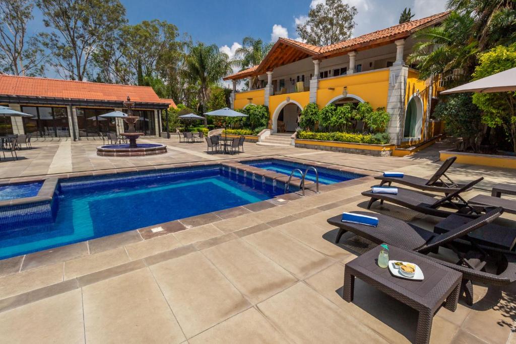 a swimming pool with chairs and a house at Hotel Hacienda Montesinos in Morelia