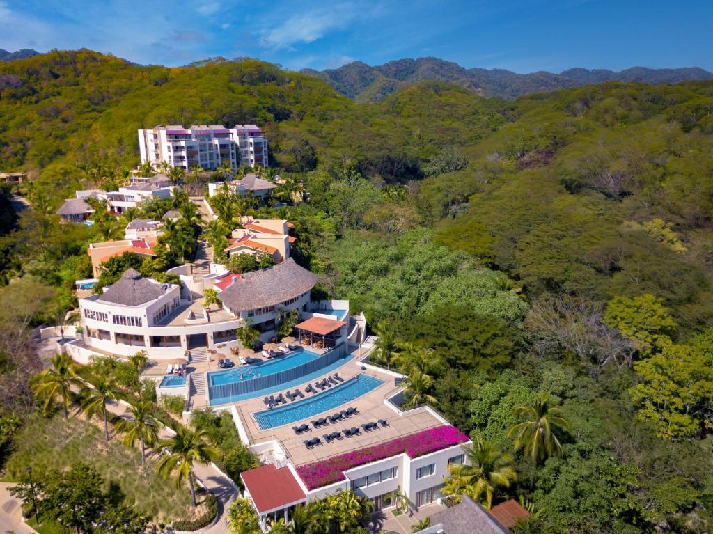 Aerial view of resort complex with pools, buildings, and surrounding green mountains.
