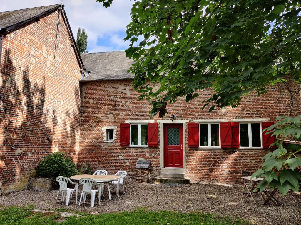 ein Backsteinhaus mit einer roten Tür sowie einem Tisch und Stühlen in der Unterkunft Uw eigen boerderij bij Le Moulin de la Place in Hargicourt