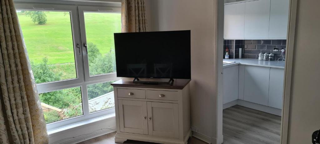 a television on a cabinet in a kitchen with a window at Espedair Apartment in Paisley