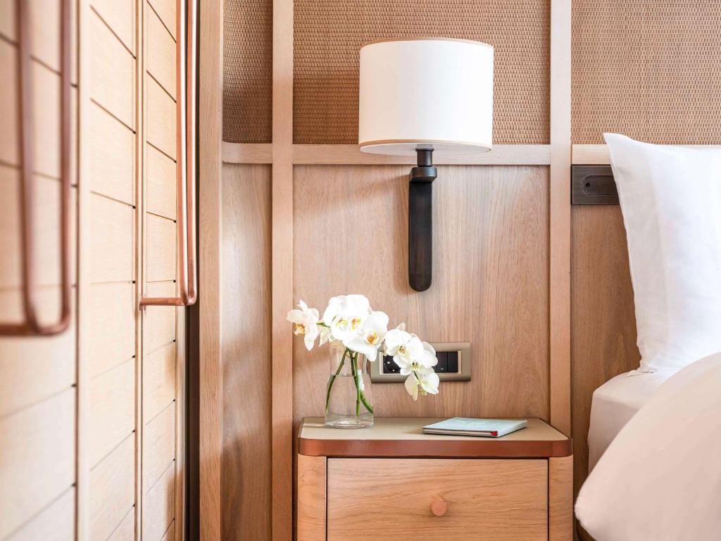 a vase of flowers on a table next to a bed at The Bodrum Hotel Yalikavak - MGallery Collection in Yalıkavak