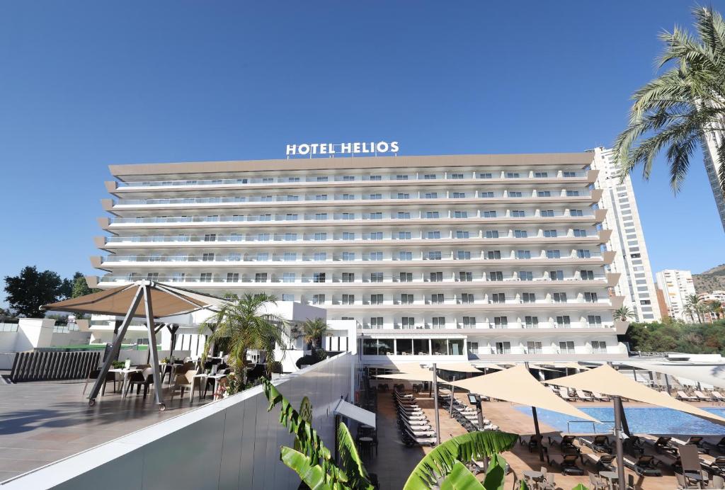 a hotel with tables and umbrellas in front of it at Helios Benidorm in Benidorm