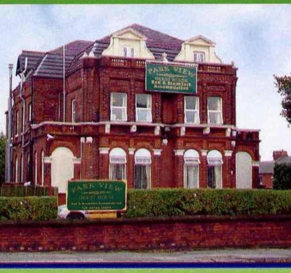 un grand bâtiment en briques avec deux panneaux devant lui dans l'établissement Park View Hotel and Guest House, à Thatto Heath