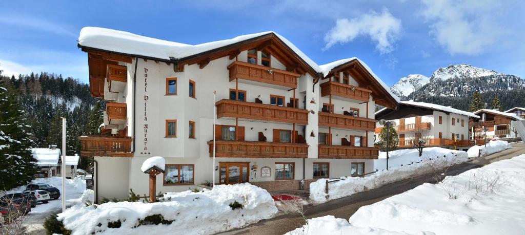 un grande edificio con neve di fronte di Hotel Villa Aurora a San Martino di Castrozza