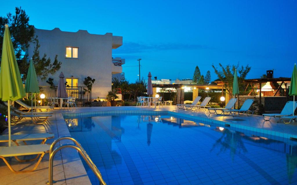 a swimming pool with chairs and umbrellas at night at Altis Hotel in Malia