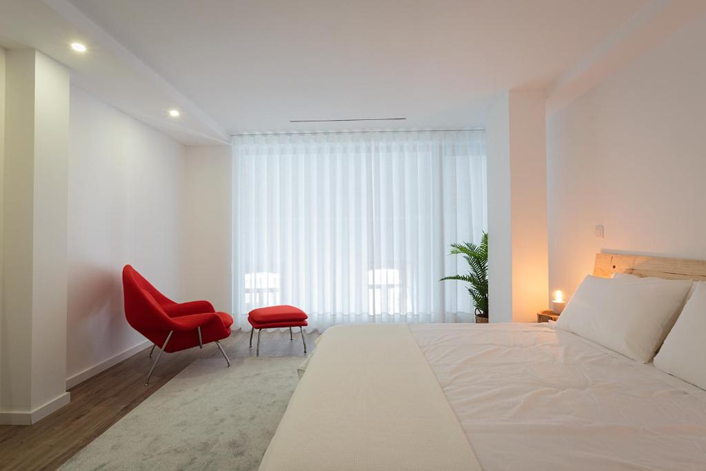 a bedroom with a large bed and a red chair at Autor Guesthouse in Vila do Conde