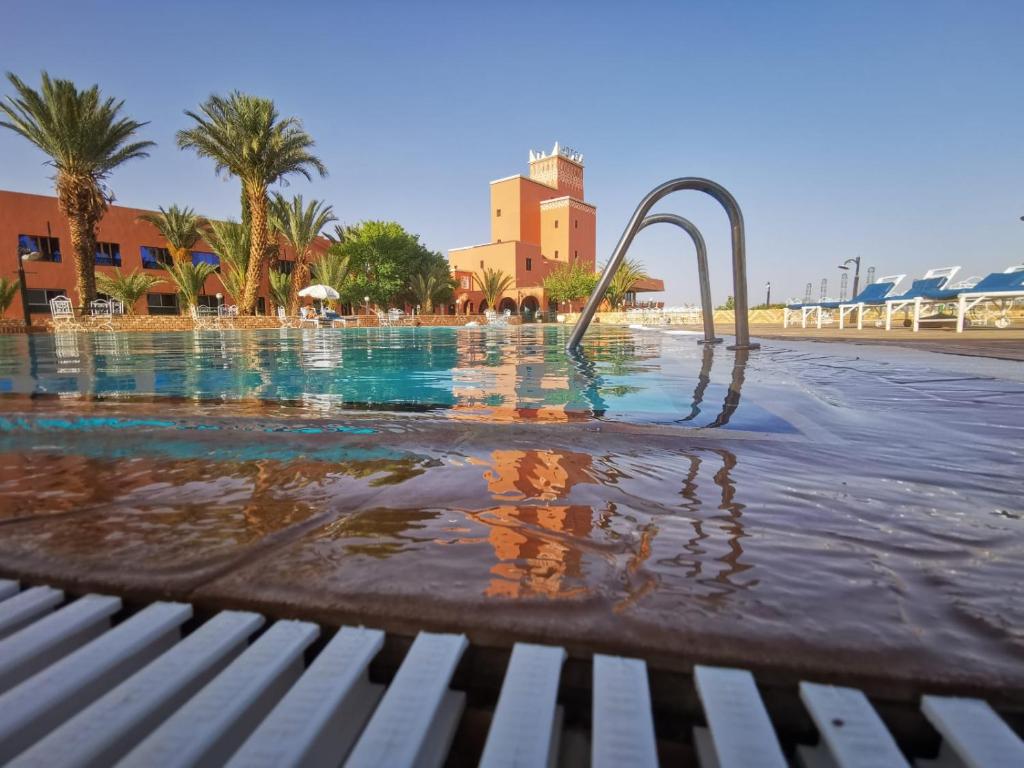 a swimming pool next to a bench and palm trees at Hotel Saghro in Tinerhir