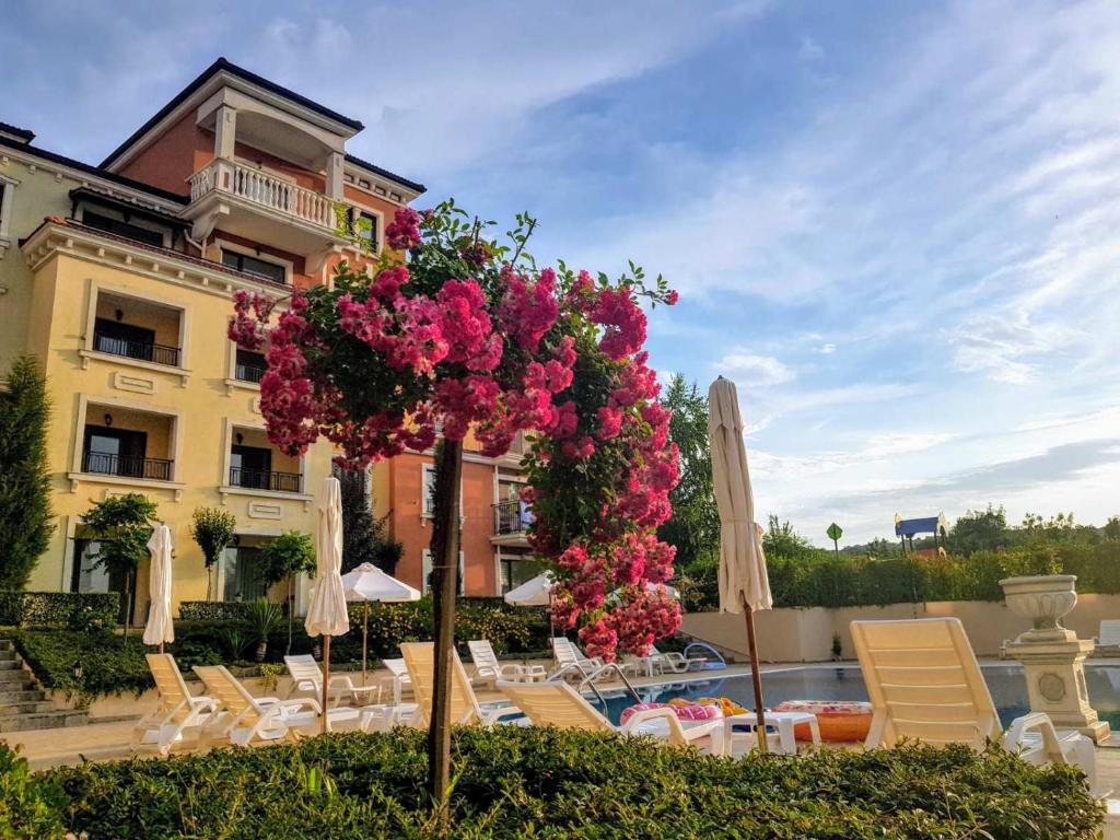 a tree with pink flowers in front of a building at Lilia Apartments Каваци, Созопол in Sozopol