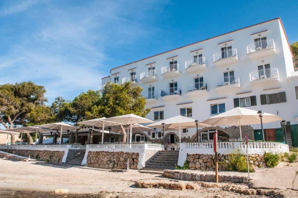 un gran edificio blanco con sombrillas delante en HOSTAL XUROY en Sant Lluís