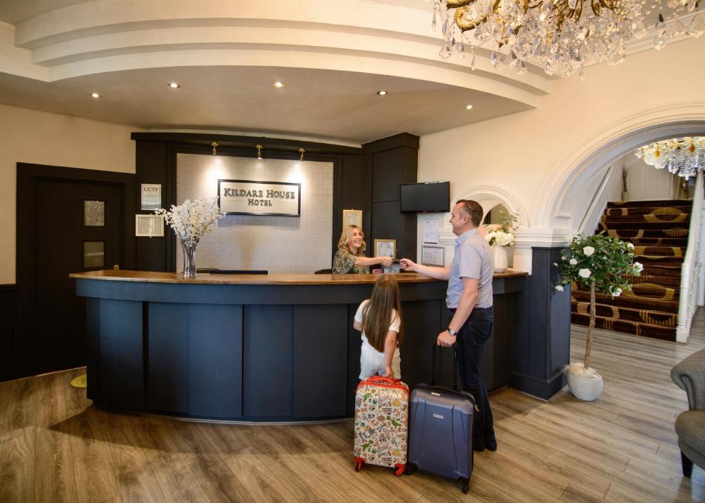 a man and a little girl standing at a counter with luggage at Kildare House Hotel in Kildare