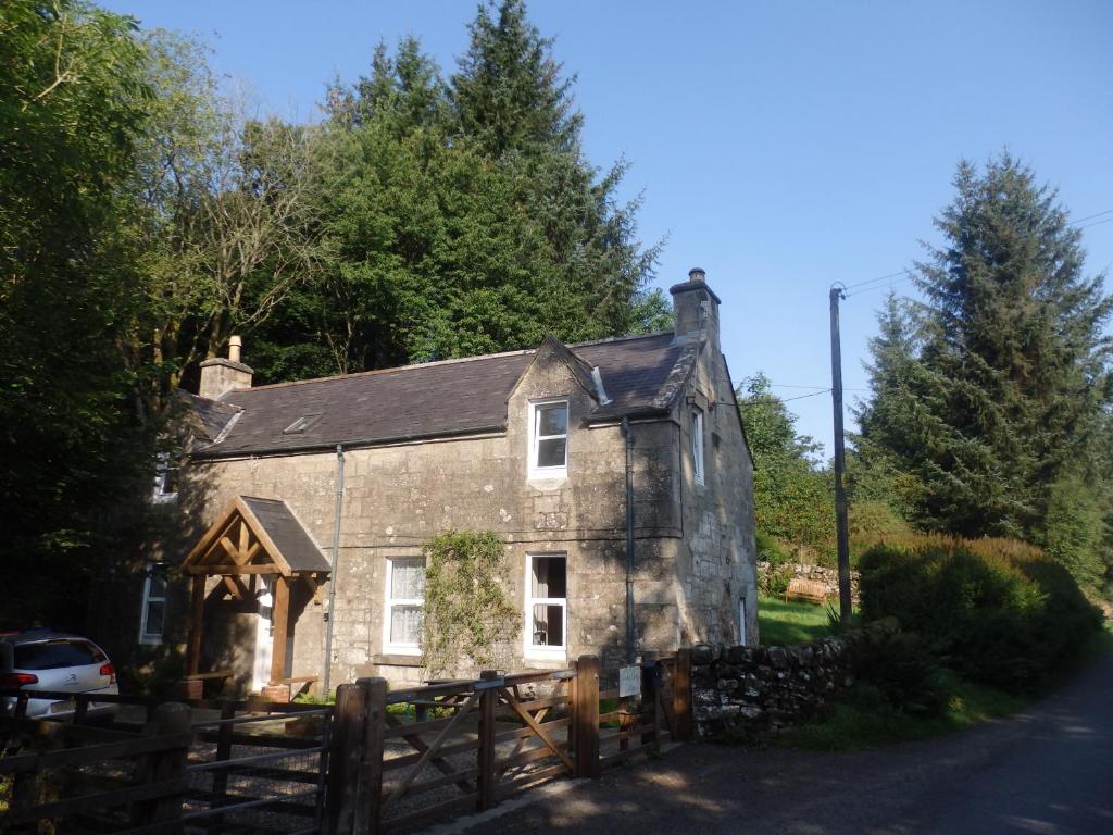 una antigua casa de piedra con una valla de madera en Lovely house next to Euchan River, en Sanquhar