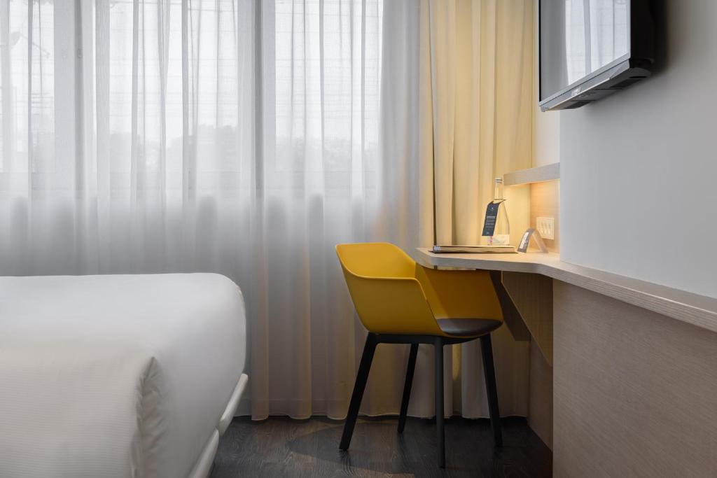 A compact desk and yellow chair sit beside a curtained window.