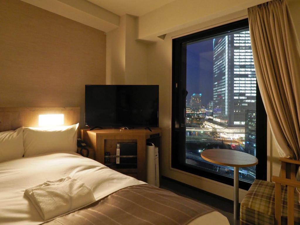 横浜市にあるファーイーストビレッジホテル横浜のベッドと大きな窓が備わるホテルルームです。