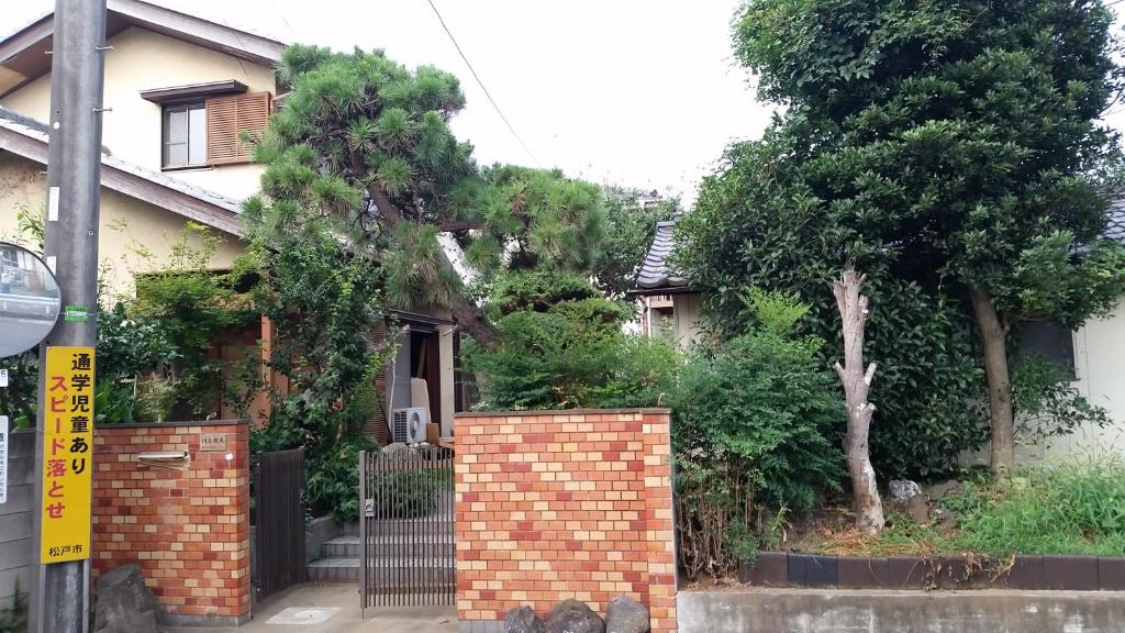 a house with a brick fence and trees at メゾン102号 Mason Guest House Suite 102 in Matsudo