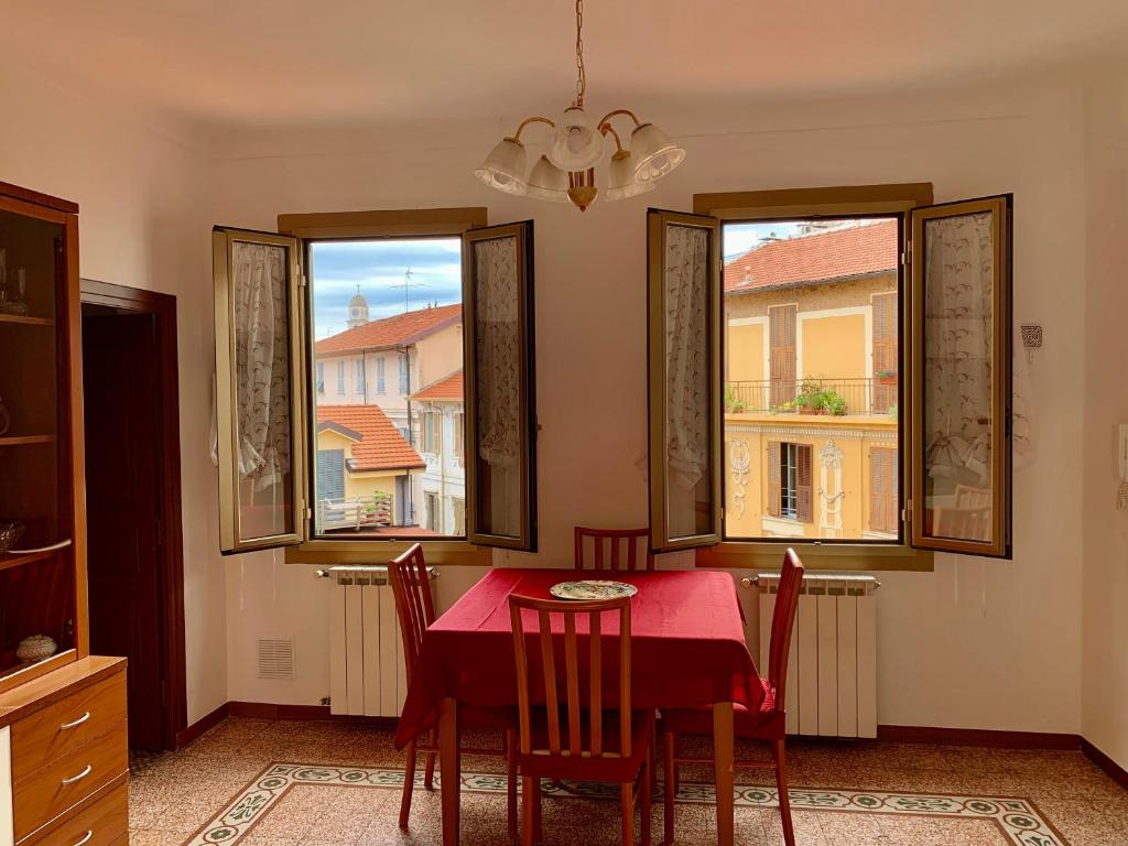 uma sala de jantar com uma mesa e cadeiras vermelhas e 2 janelas em Casa Dei Nonni em Sanremo