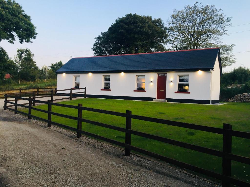 una casa blanca con techo negro y valla en Keanes Country Cottage in The Heart Of The West en Lisacul