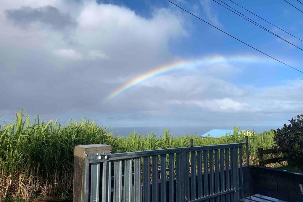 a rainbow in the sky over a wooden fence at Maison vue mer chaleureuse et confortable in Petite Île