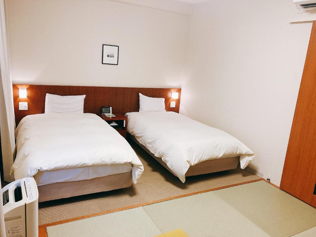 two beds in a small room with white sheets at Dormy Inn Kanazawa Natural Hot Spring in Kanazawa