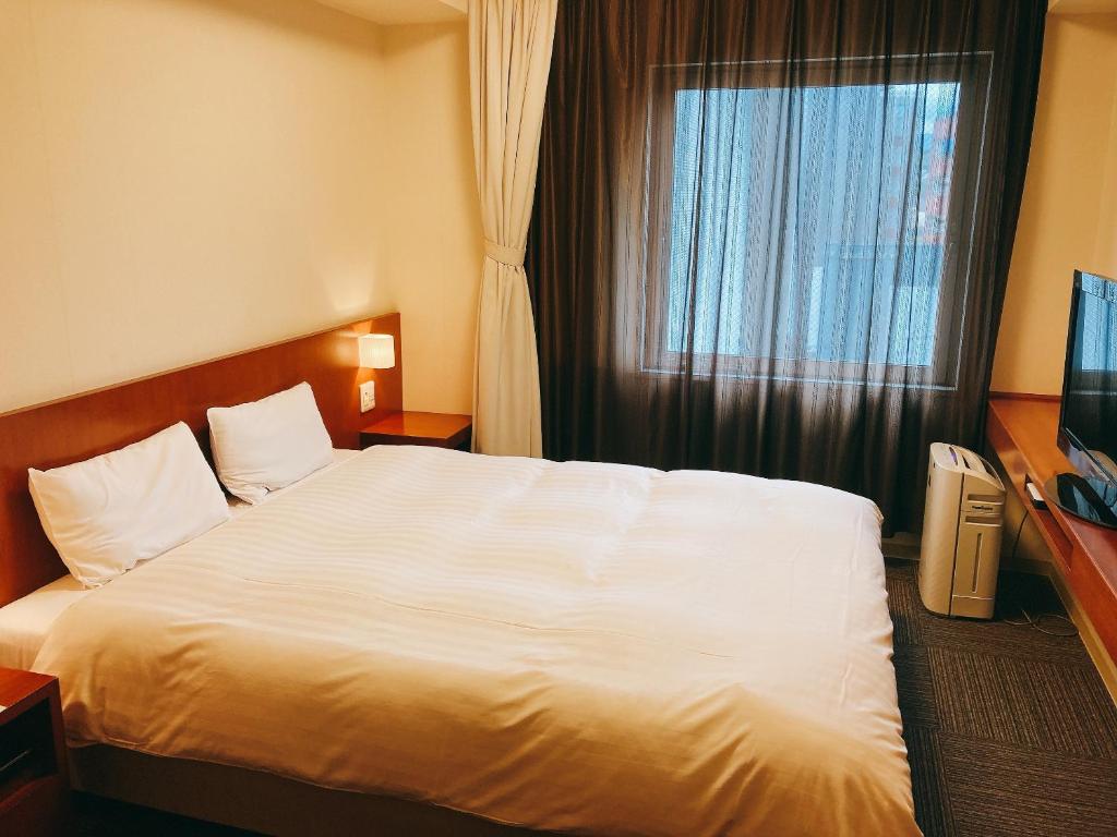 a bedroom with a large white bed and a window at Dormy Inn Kanazawa Natural Hot Spring in Kanazawa