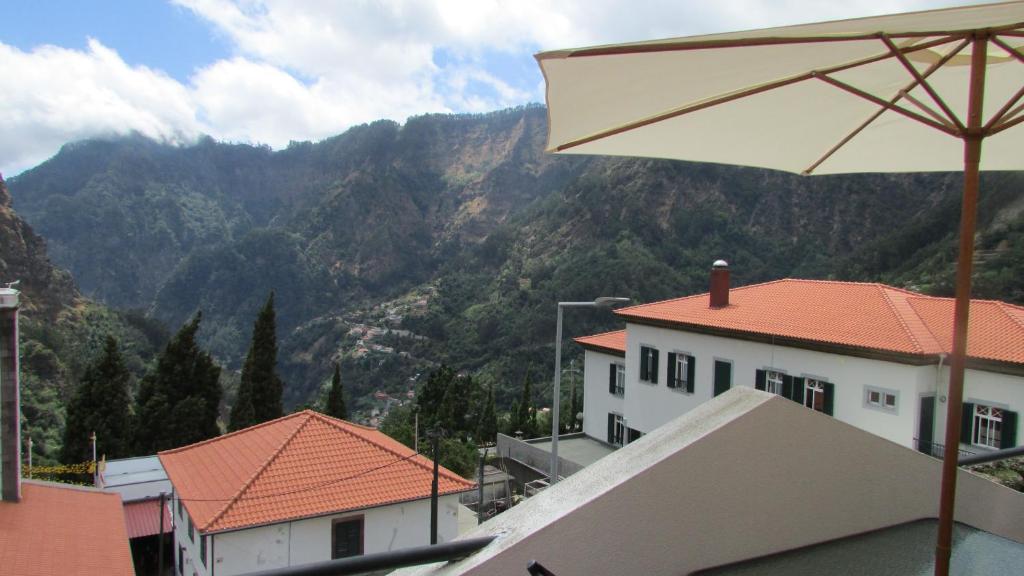 um edifício branco com um guarda-chuva em frente a uma montanha em Valley of Nuns Holiday Apartments em Curral das Freiras