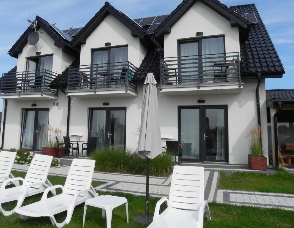 une maison avec des chaises blanches et un parasol dans l'établissement BLASK LATARNl, à Niechorze