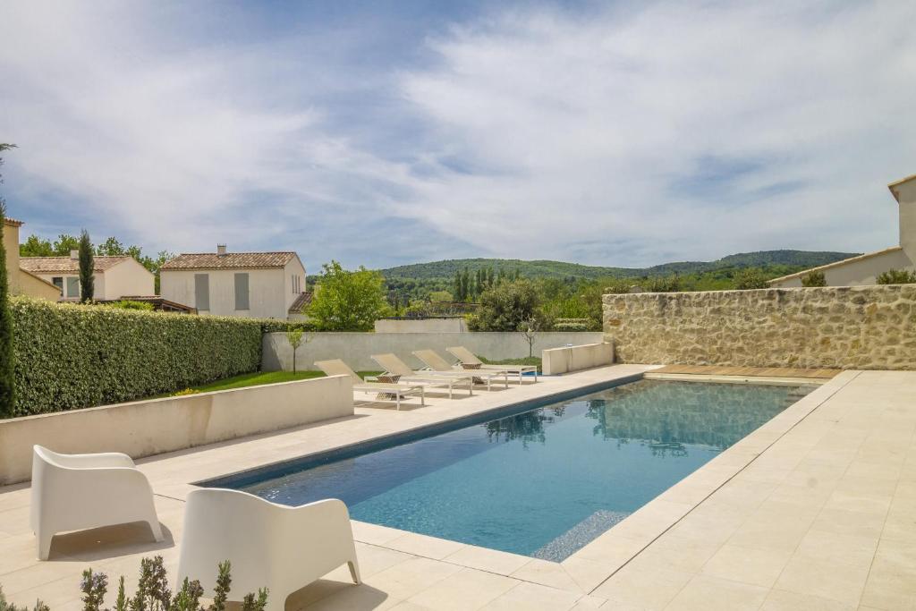 a swimming pool with white chairs and a stone wall at Au Pied du Mont Ventoux in Malaucène