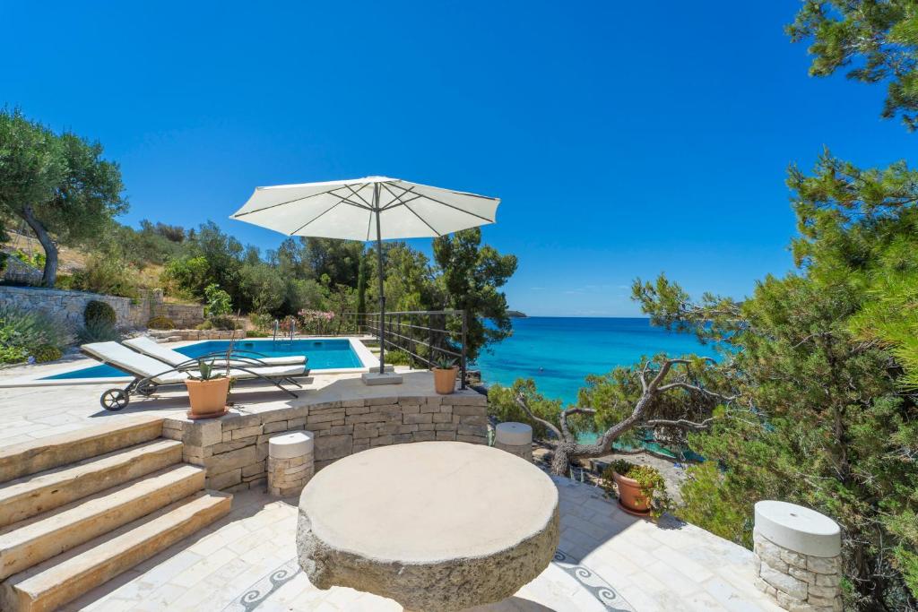 un patio con una mesa y una sombrilla y el océano en Vila Perla, en Vela Luka