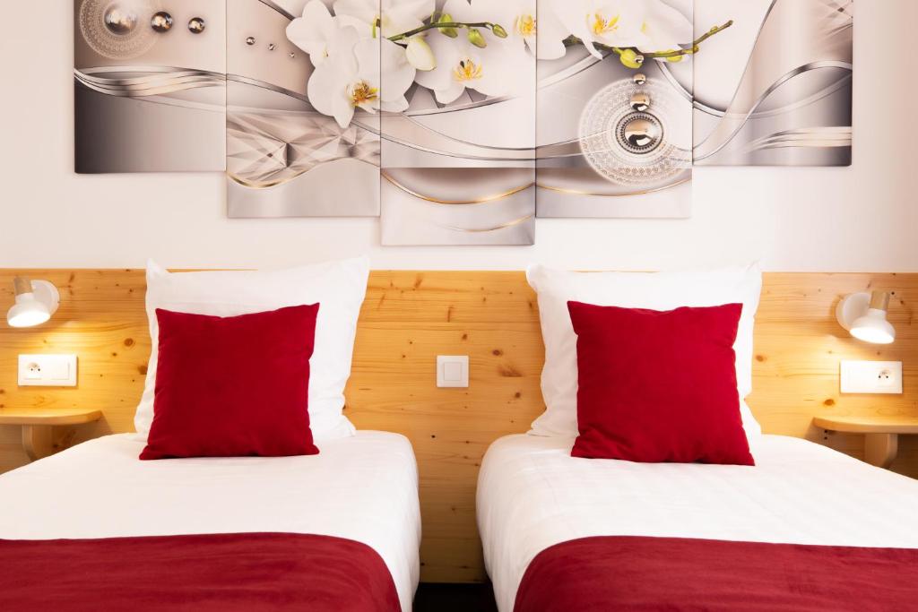 two beds in a hotel room with red pillows at hotel le beauséjour in Langogne