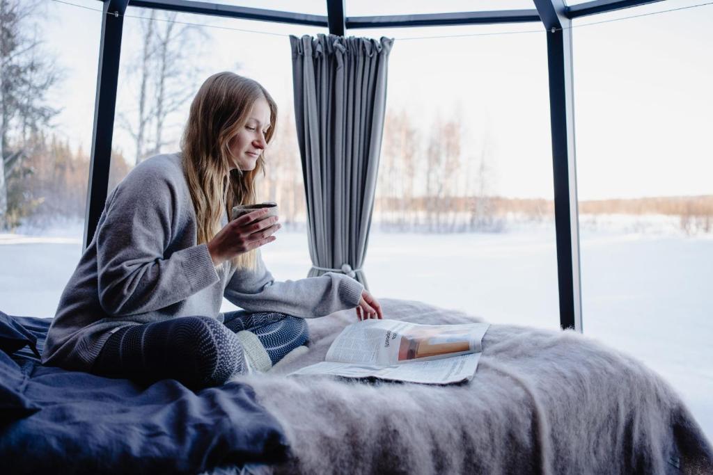 Eine Frau, die auf einem Bett sitzt und ihr Handy ansieht. in der Unterkunft Ollero Eco Lodge (including a glass igloo) in Rovaniemi