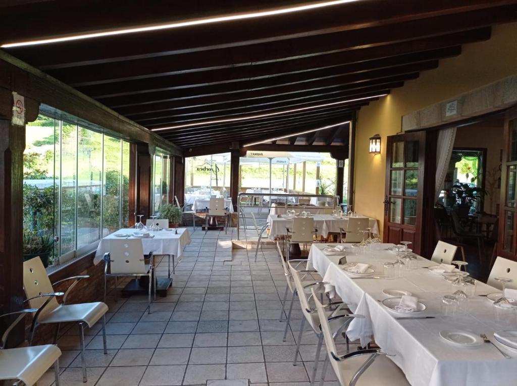 a restaurant with white tables and chairs and windows at El Tejo de Comillas in Comillas
