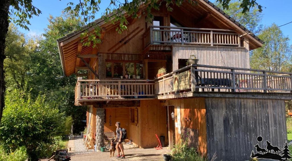 Cette cabane en rondins dispose d'un balcon et de personnes debout à l'extérieur. dans l'établissement Les deux loups, à Samoëns