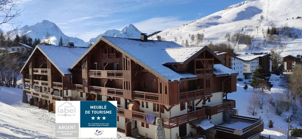 un edificio en la nieve con un cartel delante en T2 Meublé Tourisme 3 etoiles, pied des pistes-parking privé avec balcon et superbe vue en Les Deux Alpes