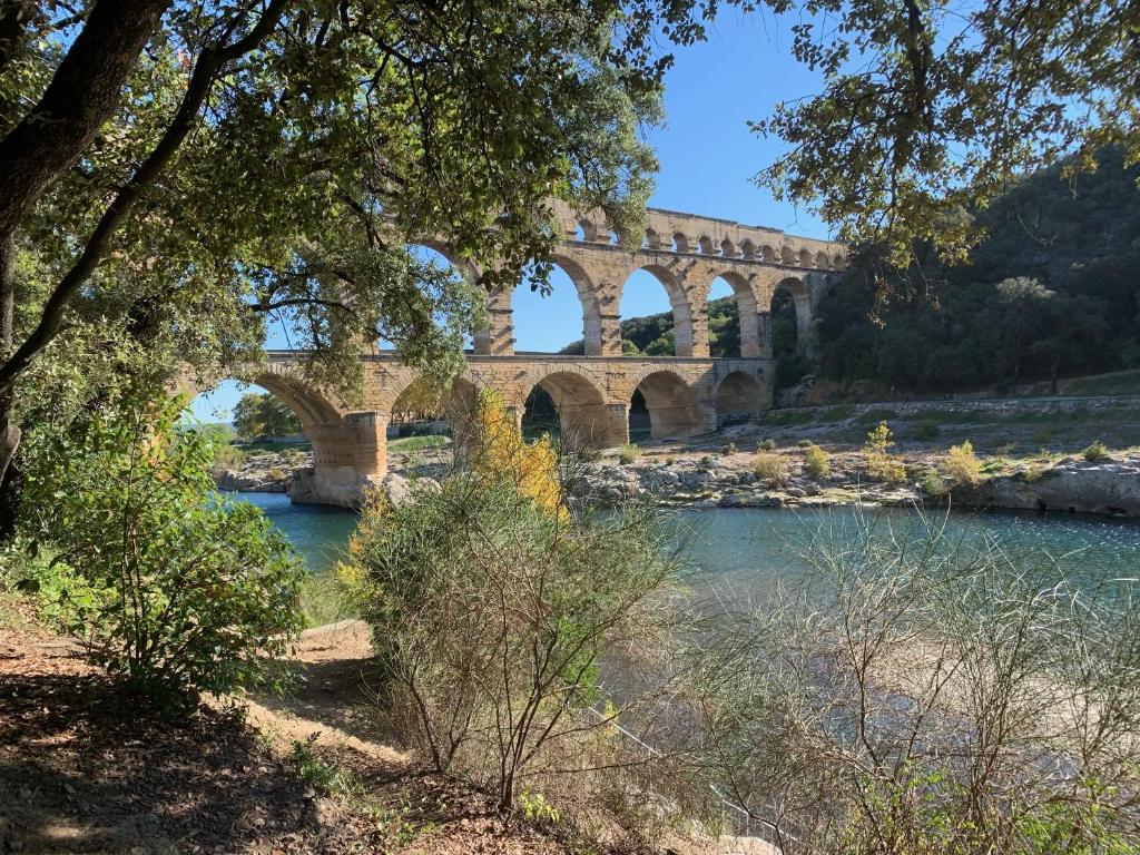 un puente sobre un río con árboles y agua en Maison de ville Pont du Gard centre historique en Remoulins