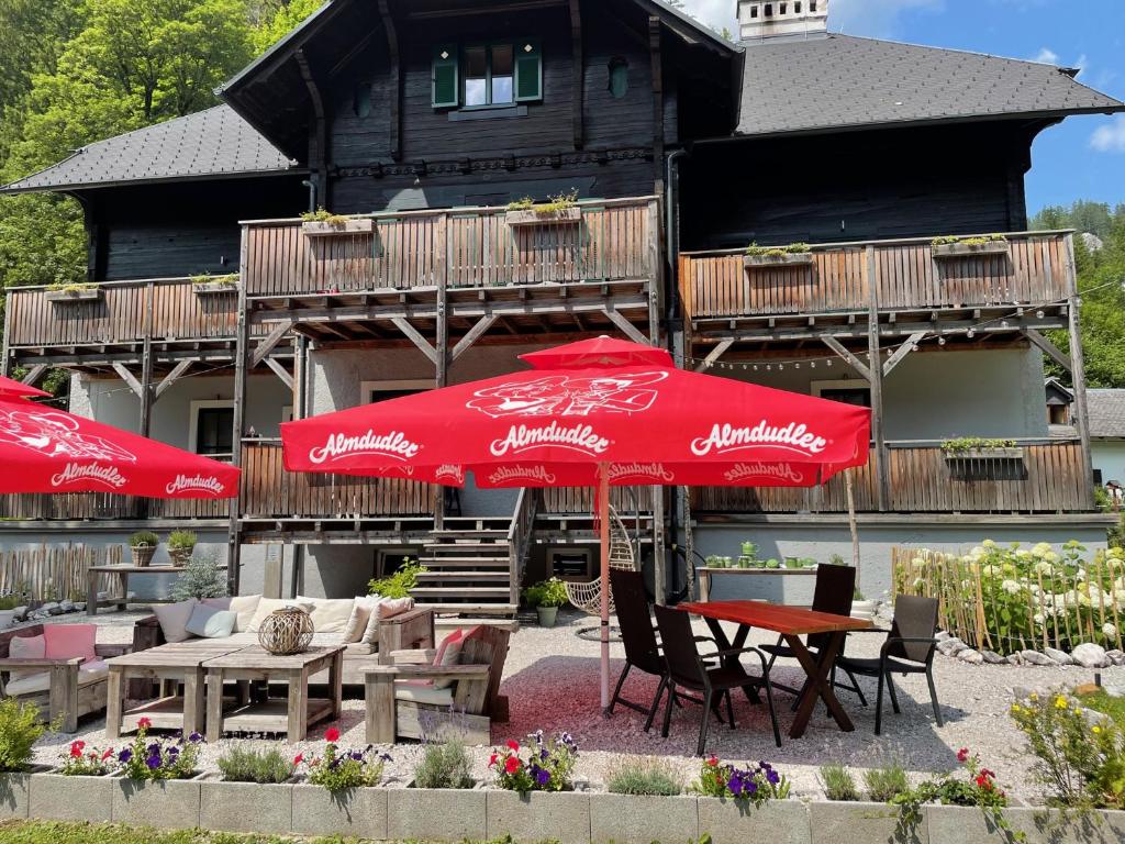 dois guarda-sóis vermelhos, mesas e cadeiras em frente a um edifício em Gesäuse-Lodge em Gstatterboden