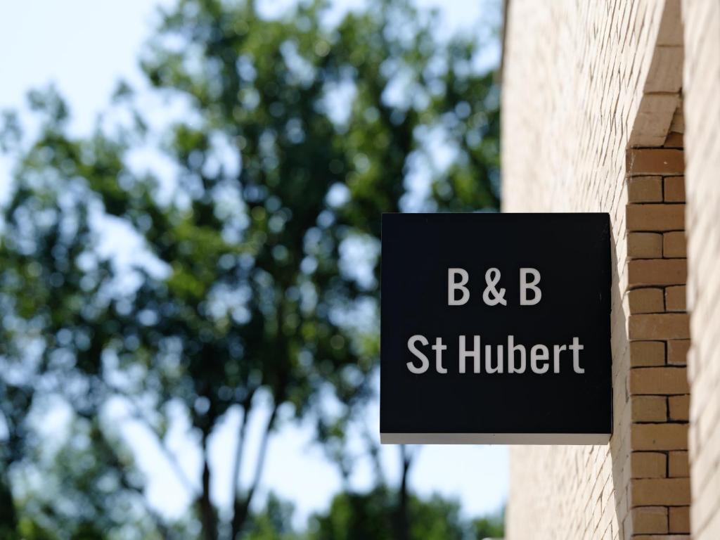 un panneau sur le côté d'un bâtiment avec des arbres en arrière-plan dans l'établissement b & b St-Hubert, à Sint-Martens-Lennik