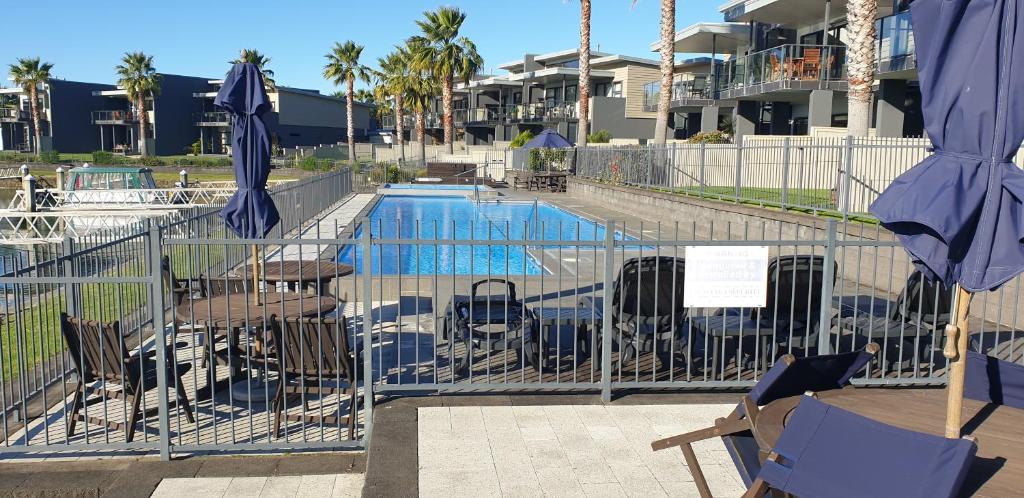 a swimming pool with chairs and umbrellas next to a fence at Waterways Renaissance "A Touch Of Class" in Whitianga