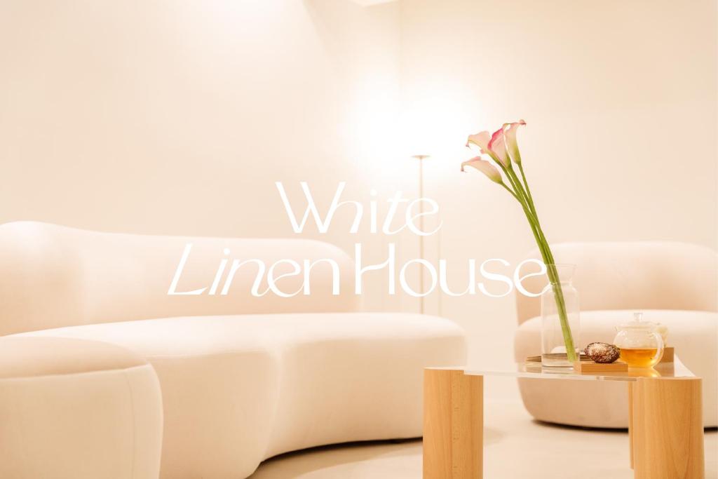 a white living room with a white leather couch and a table with a flower at White Linen House in Seoul