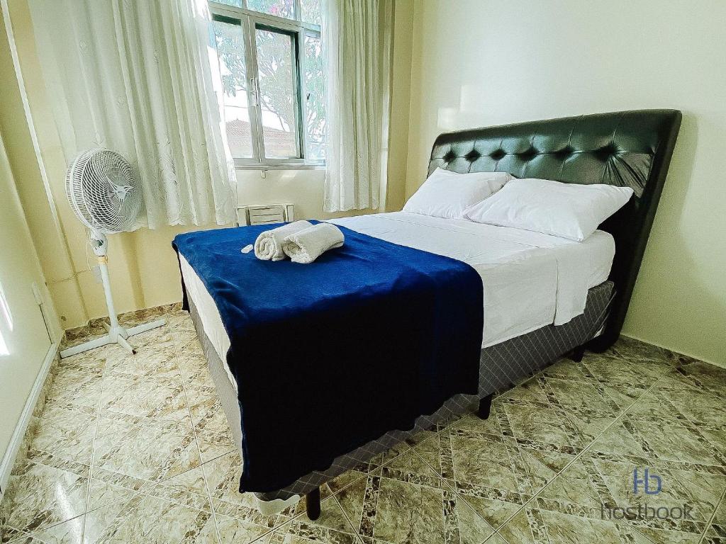 a bedroom with a bed with a blue blanket and a fan at Apto a 400 m da praia do Centro - WIFI 200MB - TV Smart - Cozinha equipada - Garagem - Ar condicionado in Rio das Ostras