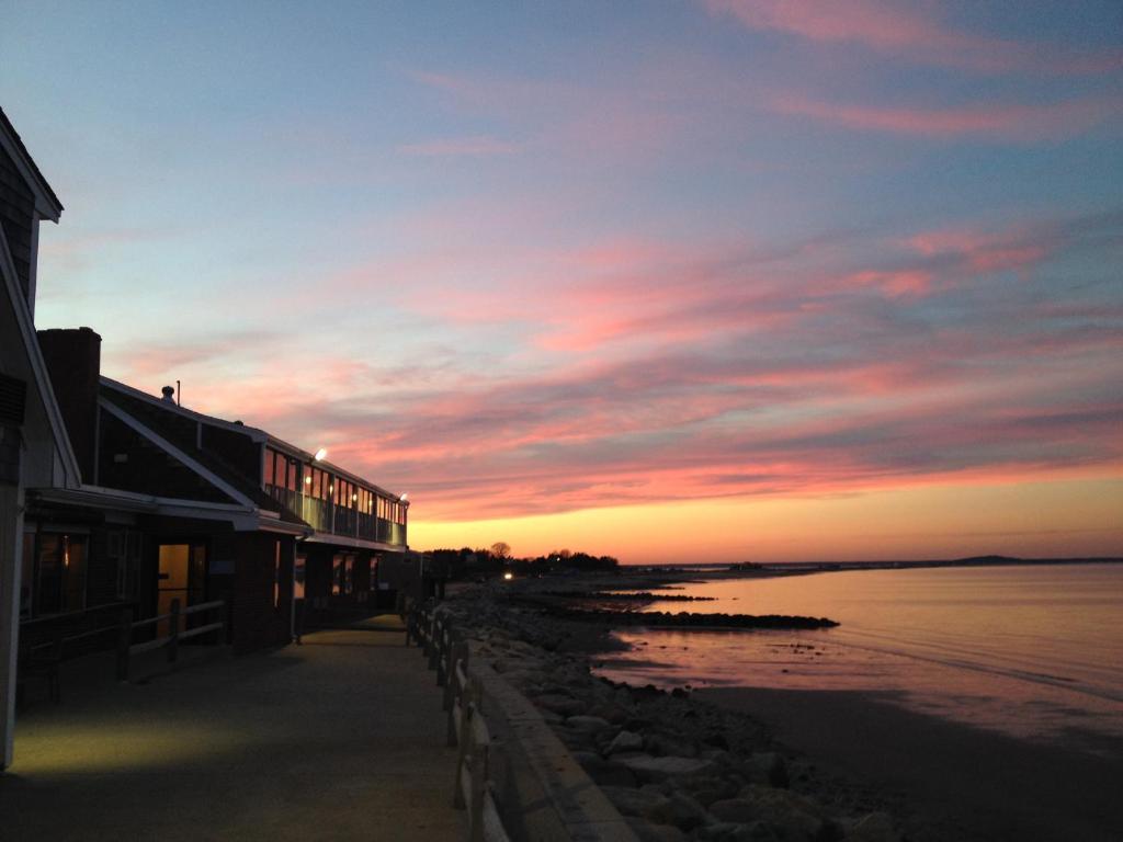 zachód słońca nad plażą z budynkiem i oceanem w obiekcie Pilgrim Sands on Long Beach w mieście Plymouth