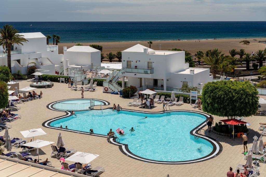 
a beach area with a pool, beach chairs, and tables at Hotel Lanzarote Village in Puerto del Carmen
