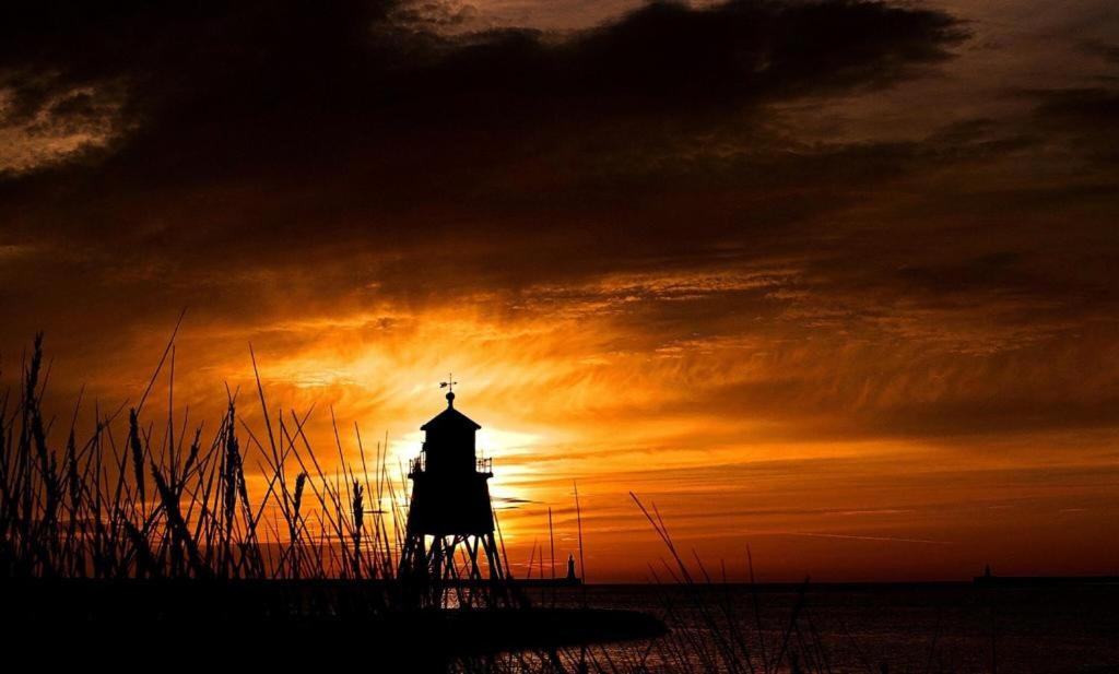 una silueta de un faro con una puesta de sol en el fondo en Cosy Haven en South Shields