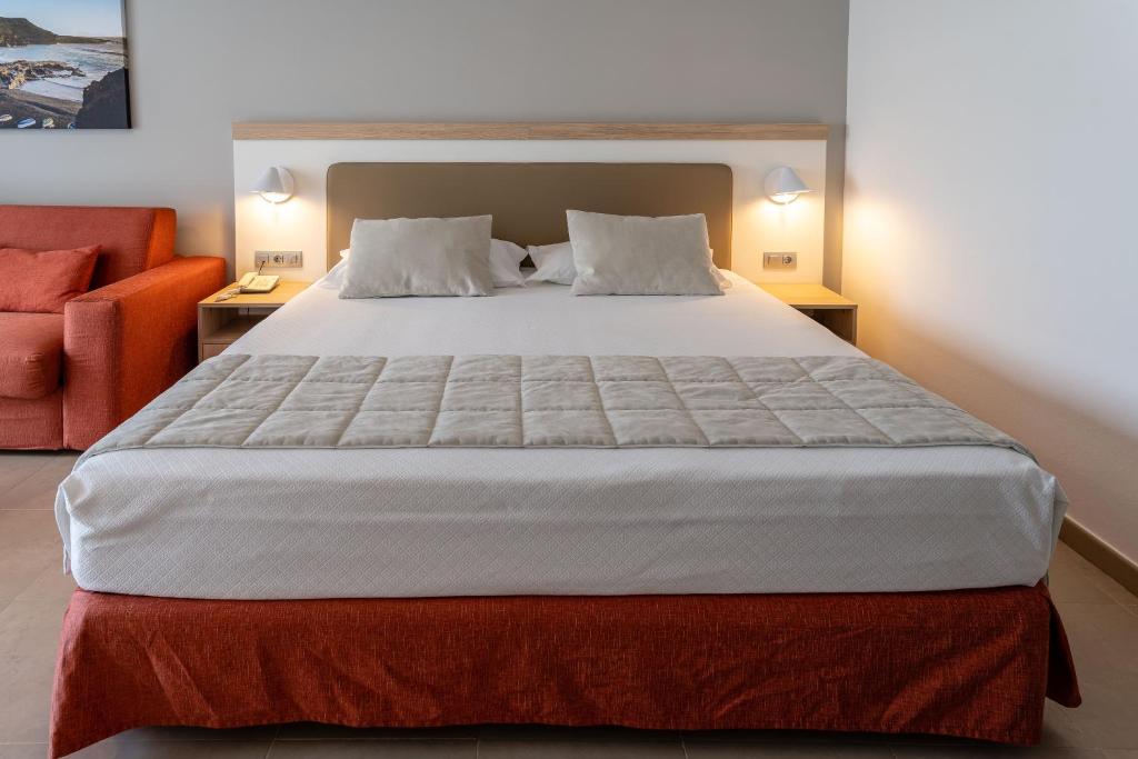 a bedroom with a large bed and a orange chair at Hotel Lanzarote Village in Puerto del Carmen