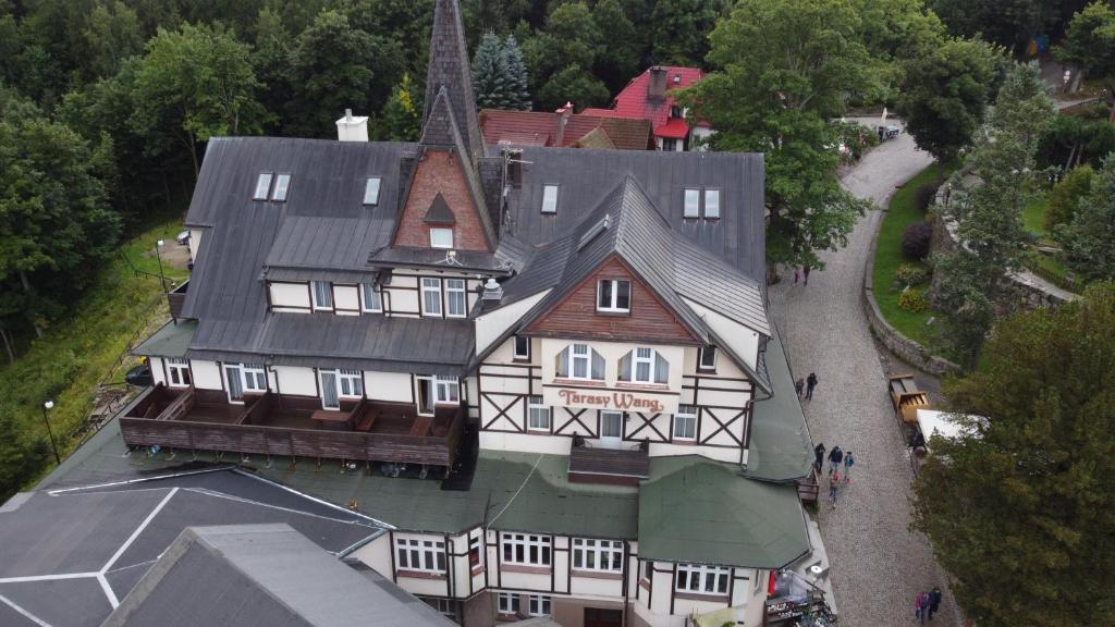 Aerial view of timber-framed mountain hotel with tall spire, tree-lined grounds, cobblestone path and small groups.