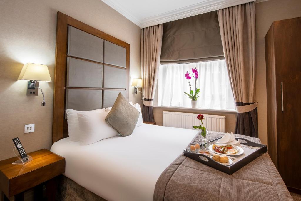 a hotel room with a bed with a tray of food on it at Gem Langham Court Hotel in London