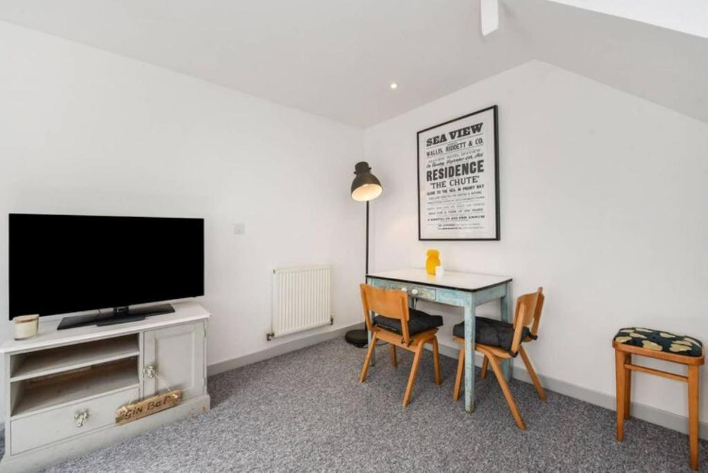 a living room with a tv and a table with chairs at The Little House, boutique home near the sea in Chichester
