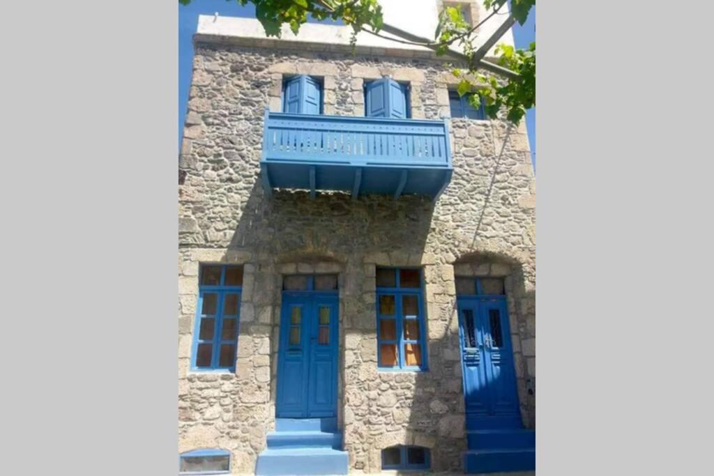 kamienny budynek z niebieskimi drzwiami i balkonem w obiekcie Imerios Nisyrian House w mieście Mandrákion