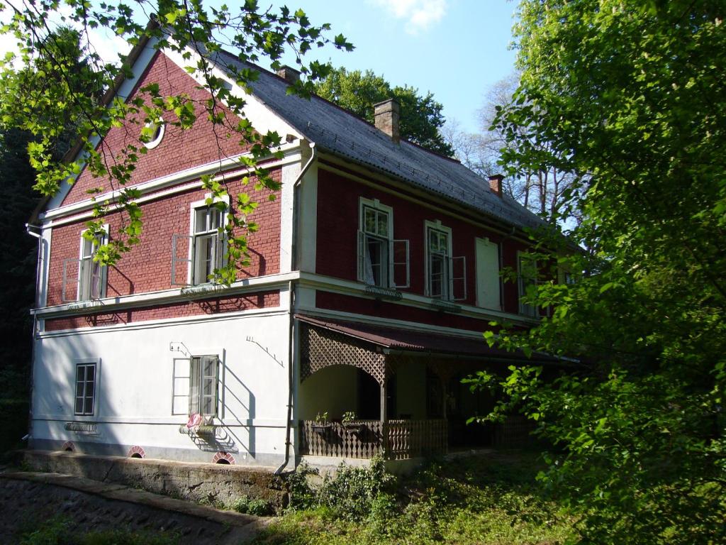 una antigua casa roja y blanca con árboles en Kalmár Vendégház-Vadászház en Tornyiszentmiklós