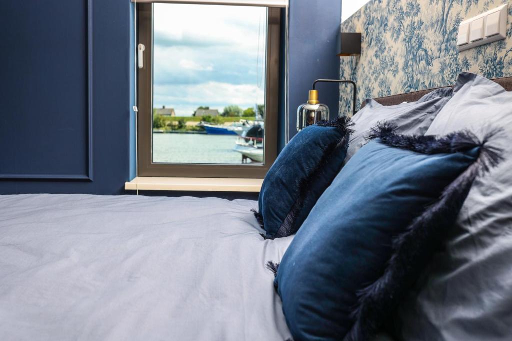 a bed with blue pillows in a room with a window at Heeren aan de Haven in Streefkerk