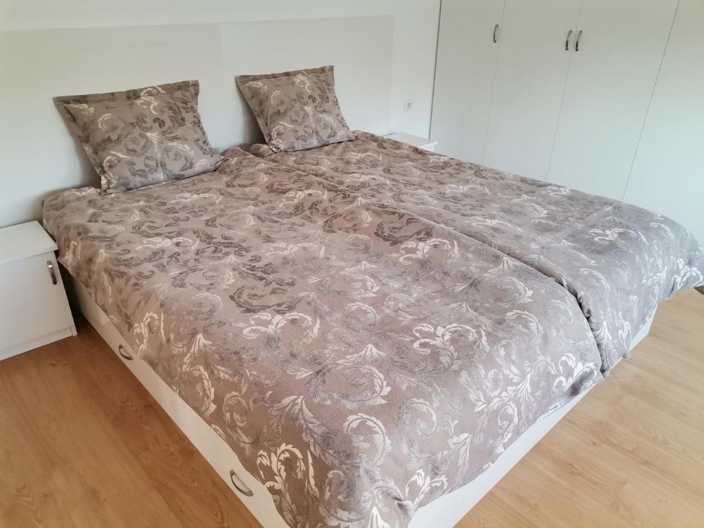a large bed with a gray blanket and pillows at Апартамент Стил in Velingrad